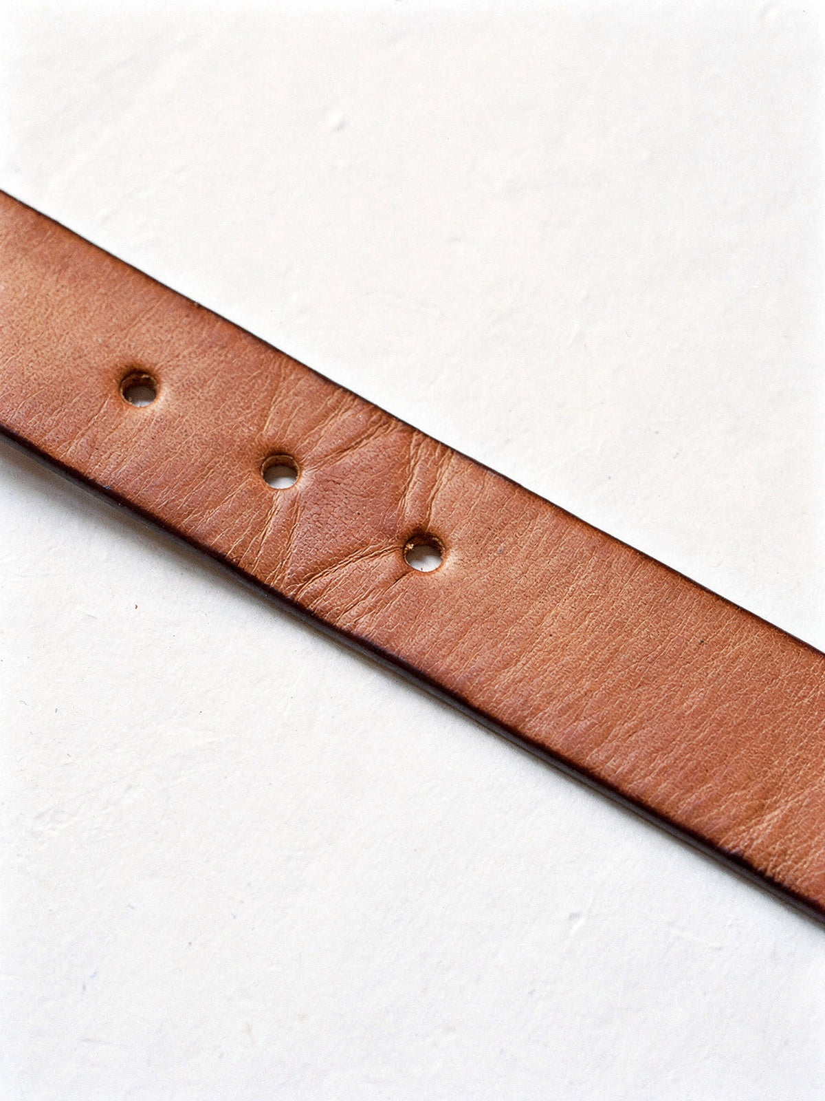 Close up of the cow leather strap of a jeans belt, punched adjustment holes and burnished edge