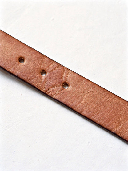 Close up of the cow leather strap of a jeans belt, punched adjustment holes and burnished edge