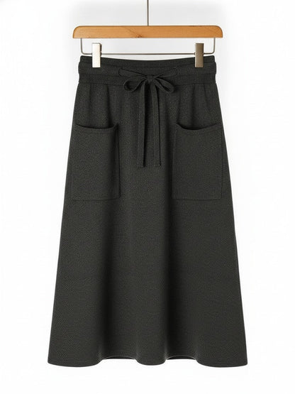 Knitted midi skirt in anthracite, a dark charcoal grey, hung flat to show the patch pockets and drawstring waist