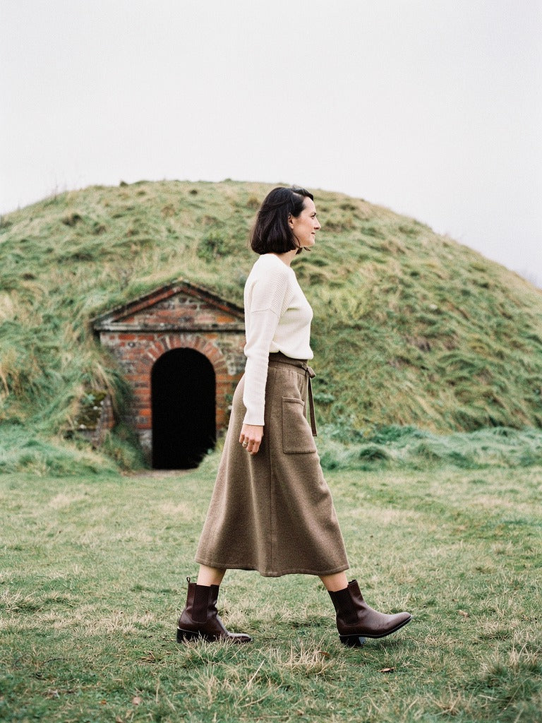 Side view of the hazelnut knitted midi skirt in wear, the hem falling at mid calf as she walks
