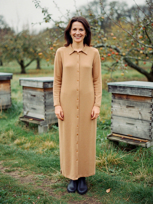 Knitted shirt dress in Biscuit worn full length beside beehives in an autumn orchard