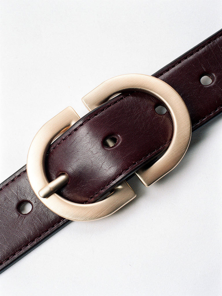 Close up of the brushed gold oval buckle, edge topstitching and punched holes of the leather belt
