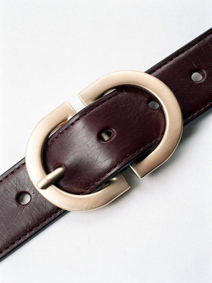 Close up of the brushed gold oval buckle, edge topstitching and punched holes of the leather belt
