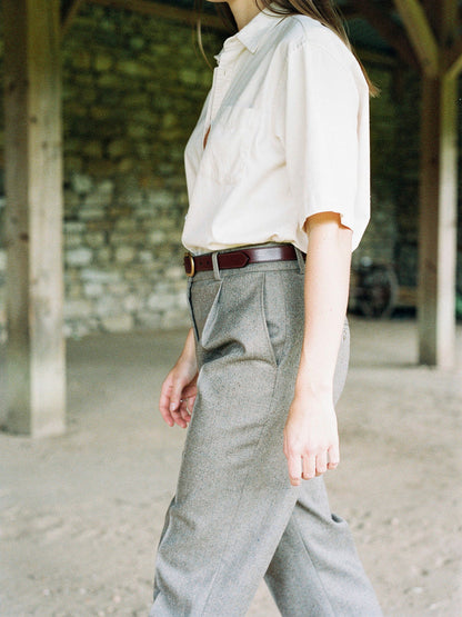 Leather belt in mahogany worn with a cream shirt and wool trousers, seen in profile