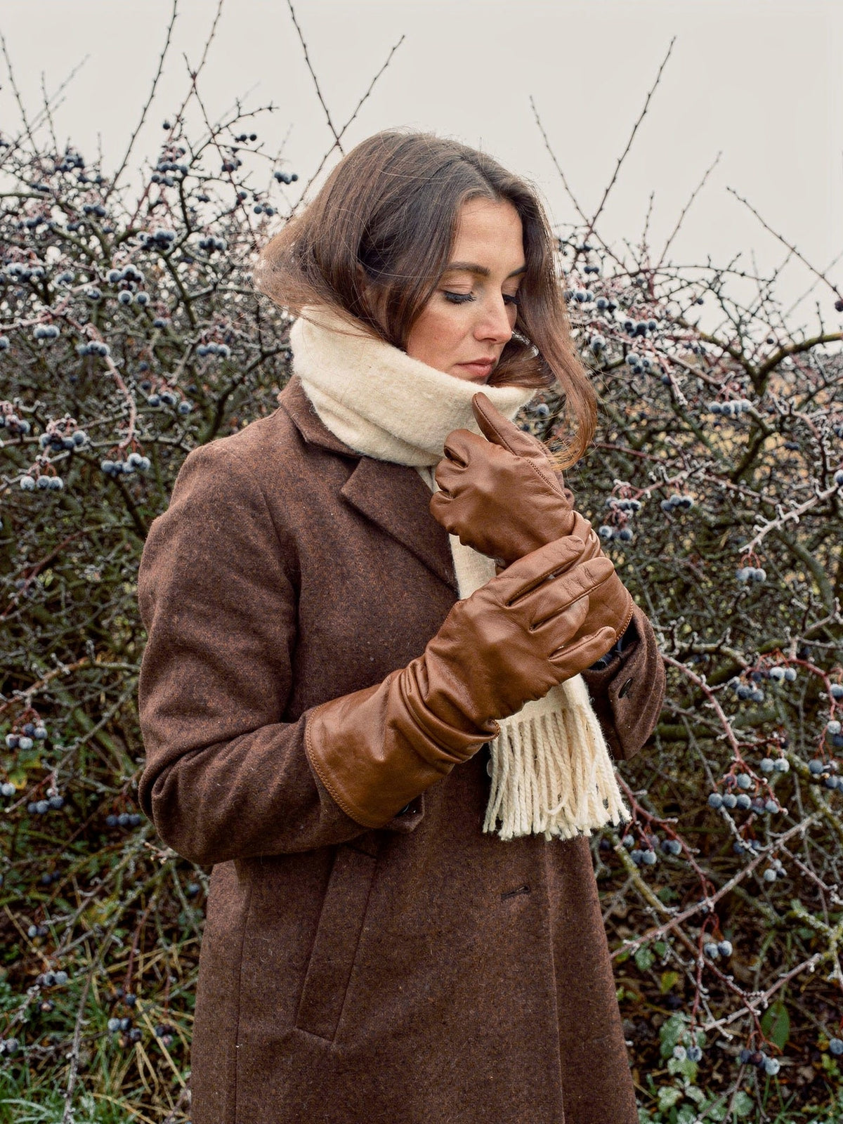 Leather gloves in Kestrel tan sheepskin worn by a frosted blackthorn hedge