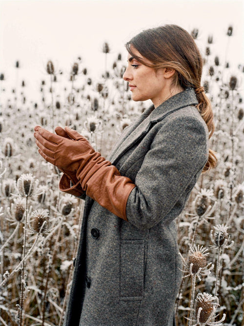 Woman wearing long leather gloves in Kestrel tan sheepskin beside frosted winter teasels
