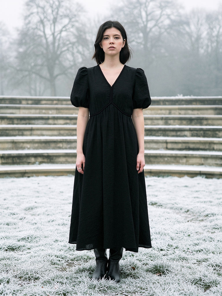 Long black dress with short puff sleeves and a deep V neck, worn full length on frosted grass in an English park
