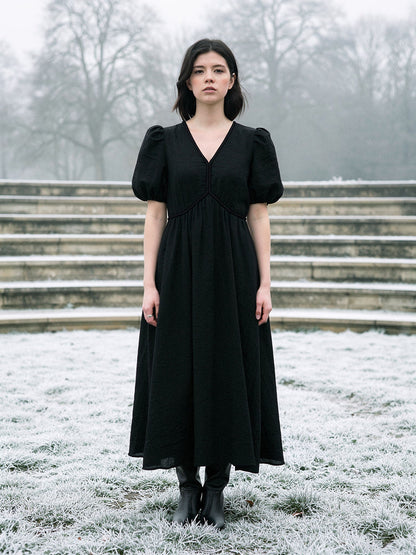 Long black dress with short puff sleeves and a deep V neck, worn full length on frosted grass in an English park