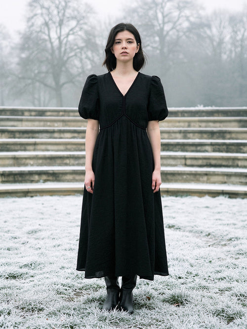 Long black dress with short puff sleeves and a deep V neck, worn full length on frosted grass in an English park