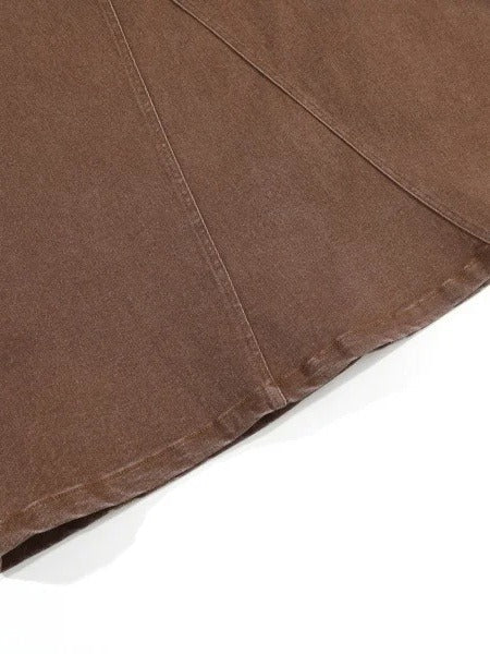 Hem of the long jean skirt in tanbark brown denim, showing the godet panel seams running into the turned and topstitched hem with no slit