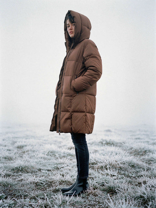 Woman wearing a brown puffer coat with the hood up on a frosted field in winter fog