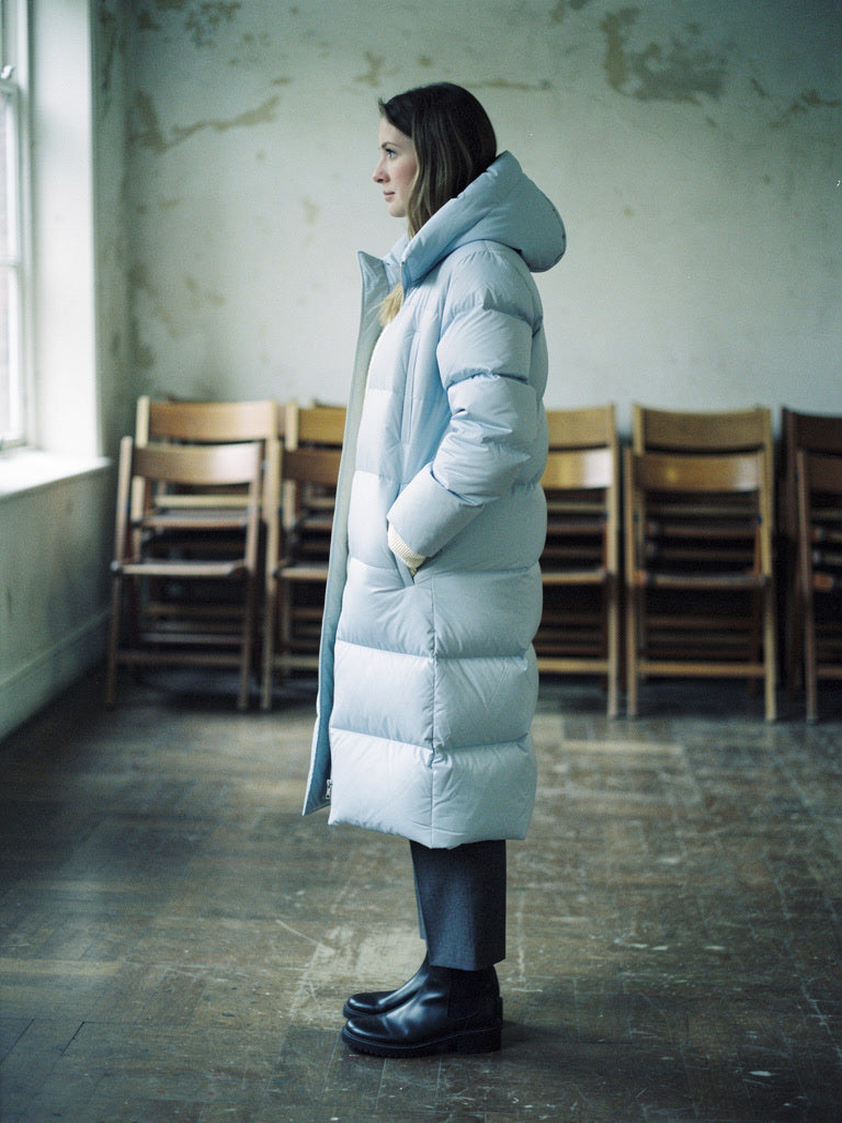 Woman wearing a long puffer coat in Ice Blue open over knitwear, side view