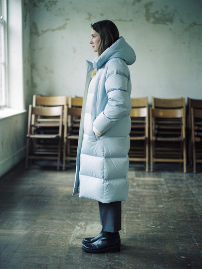 Woman wearing a long puffer coat in Ice Blue open over knitwear, side view