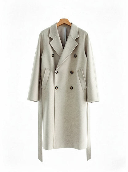 Long wool coat in Oatmeal on a hanger, double breasted with six horn buttons, slanted welt pockets and a self tie belt