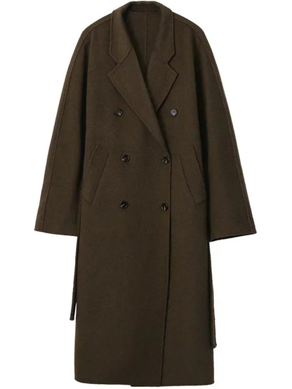 Long wool coat in Treacle on a hanger, showing the double breasted front, the welt pockets and the belt hanging loose
