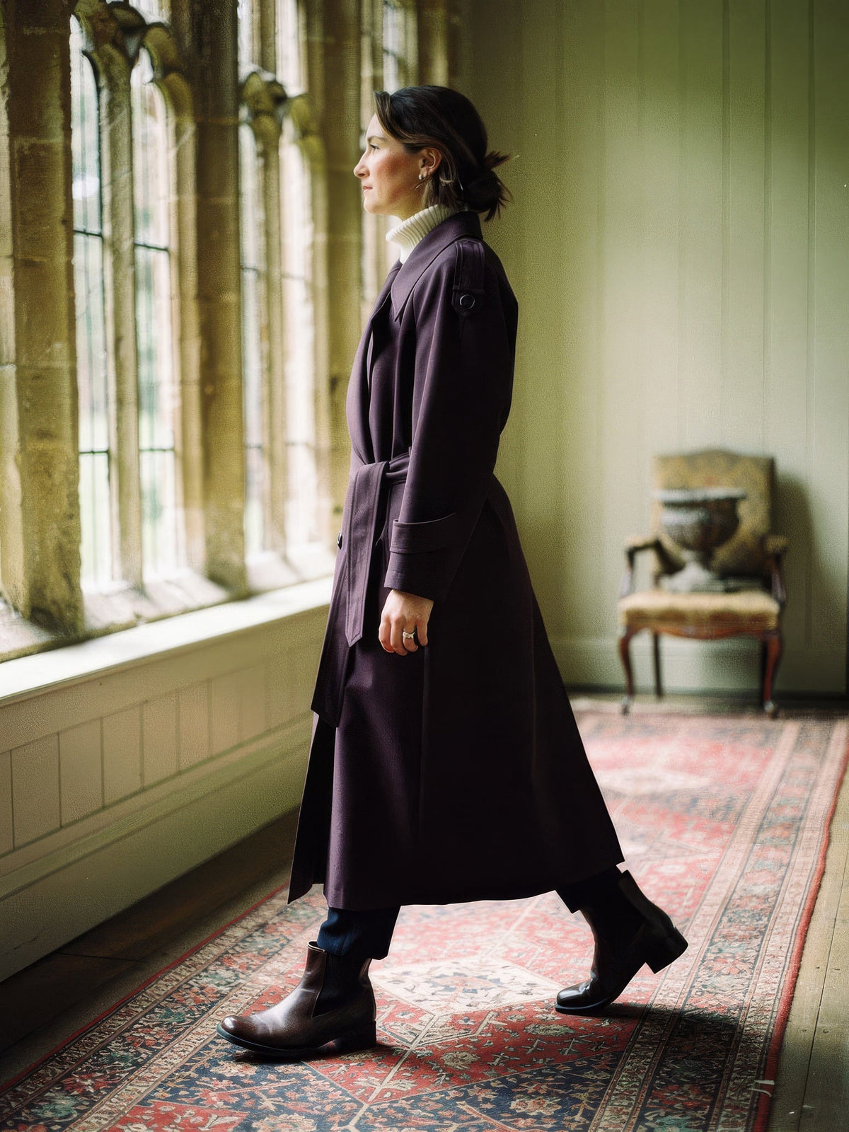 Longline trench coat in Damson worn belted, side view in a country house gallery