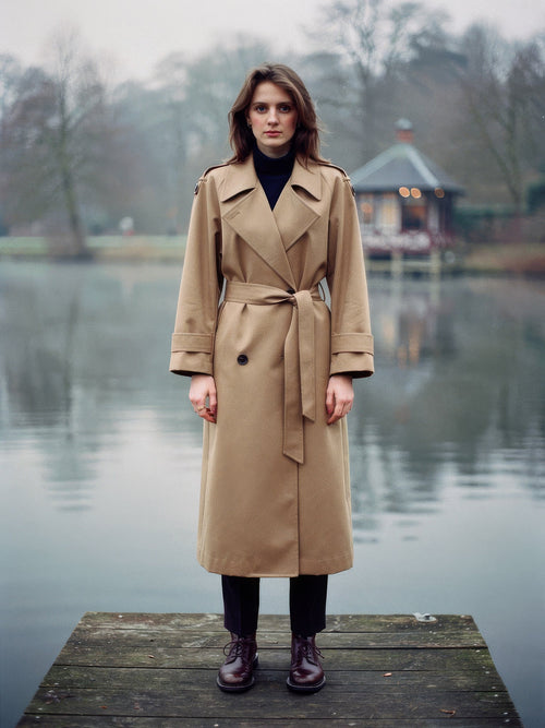 Longline trench coat in Fawn worn open on a lakeside jetty, full length