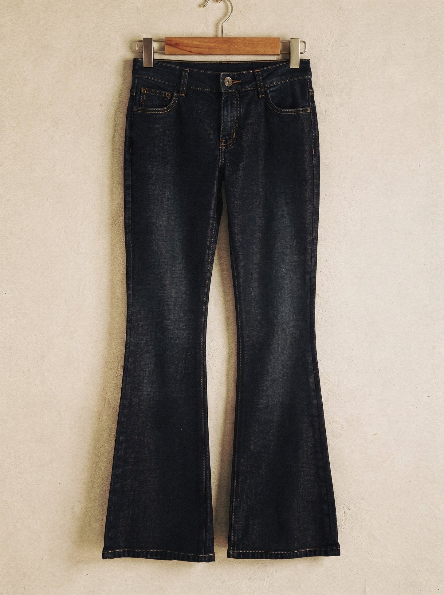 Low-rise flared jeans in dark indigo denim on a wooden hanger showing the flare from the knee