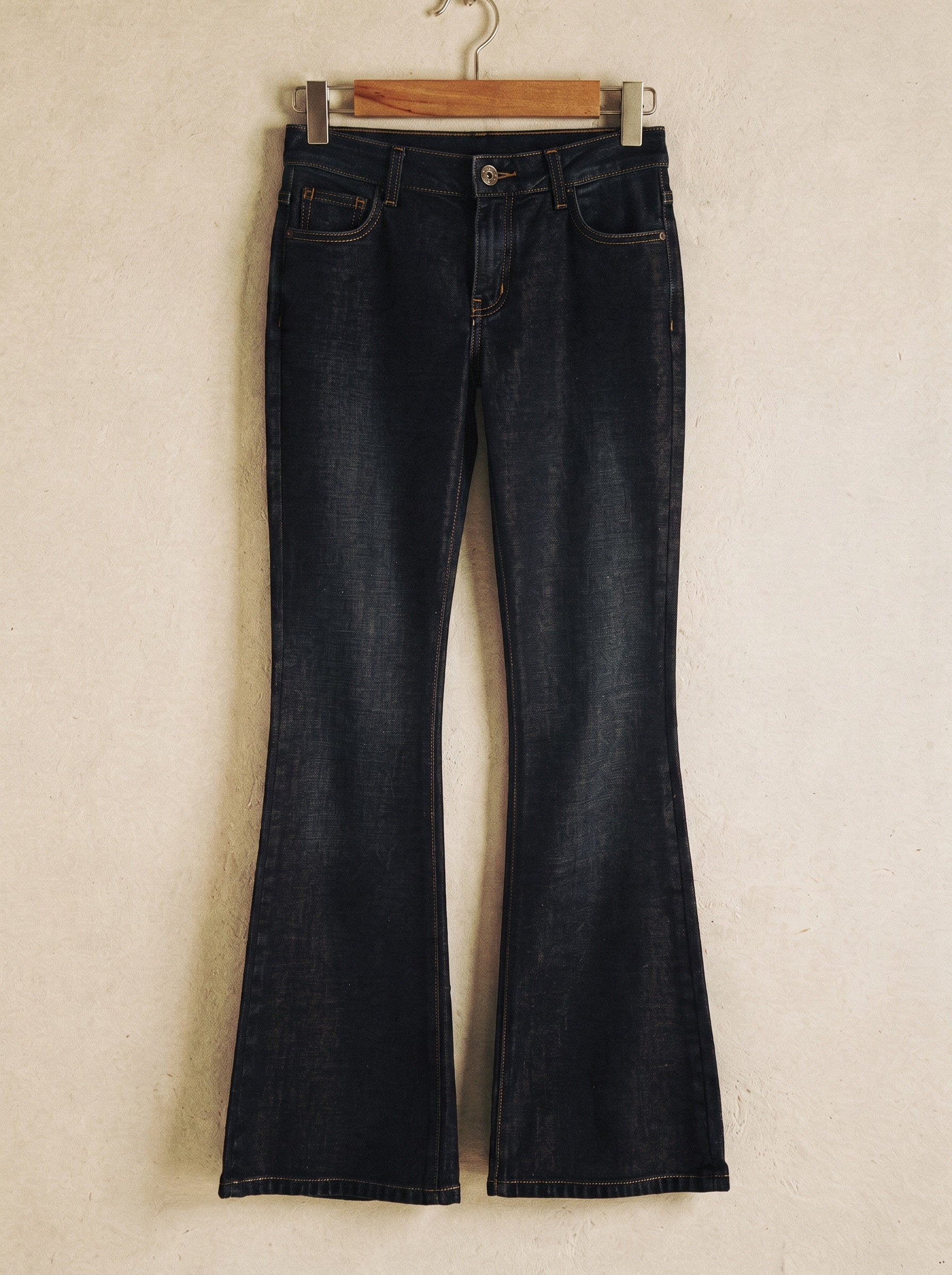 Low-rise flared jeans in dark indigo denim on a wooden hanger showing the flare from the knee