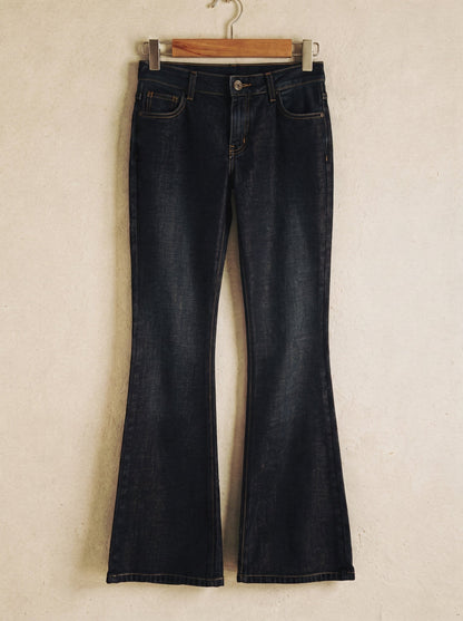 Low-rise flared jeans in dark indigo denim on a wooden hanger showing the flare from the knee