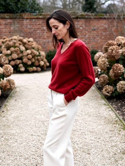 Woman wearing a Harlbury merino V-neck jumper in Poppy Red in a walled garden