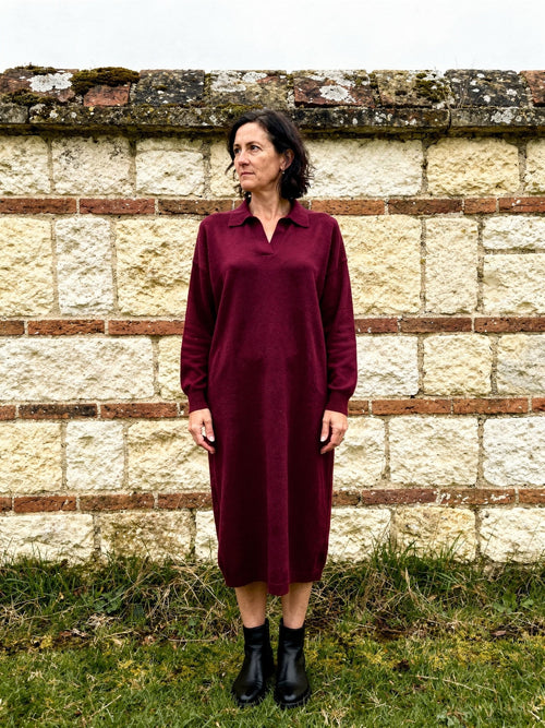 Oversized jumper dress in Claret, open collar fine rib knit, worn full length against a chalk block wall