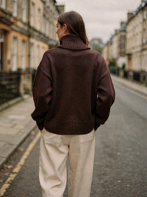 Back view of the chocolate brown oversized roll neck jumper, styled with cream trousers
