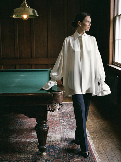 Oversized white satin blouse worn loose over slim navy trousers