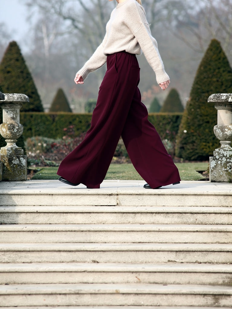 Side view of the claret palazzo trousers mid stride, the wide leg swinging open