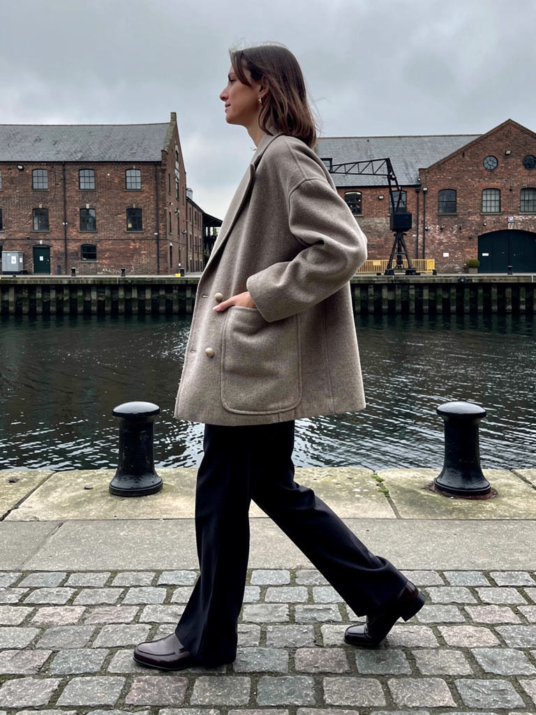 Oversized wool pea coat in Barley greige, worn on a granite dockside quay in winter