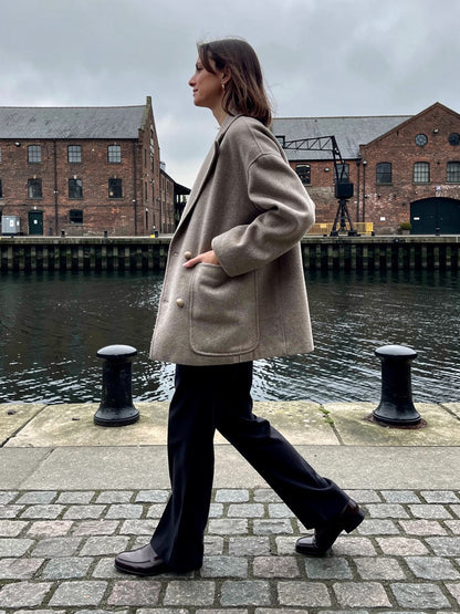 Oversized wool pea coat in Barley greige, worn on a granite dockside quay in winter