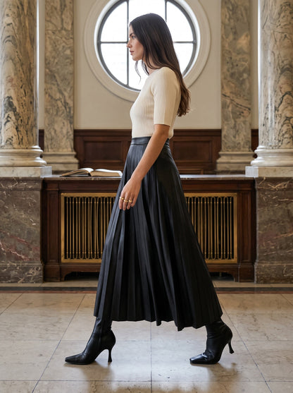 Side view of the black pleated skirt in faux leather, Rook, the knife pleats opening as she walks across an Edwardian banking hall