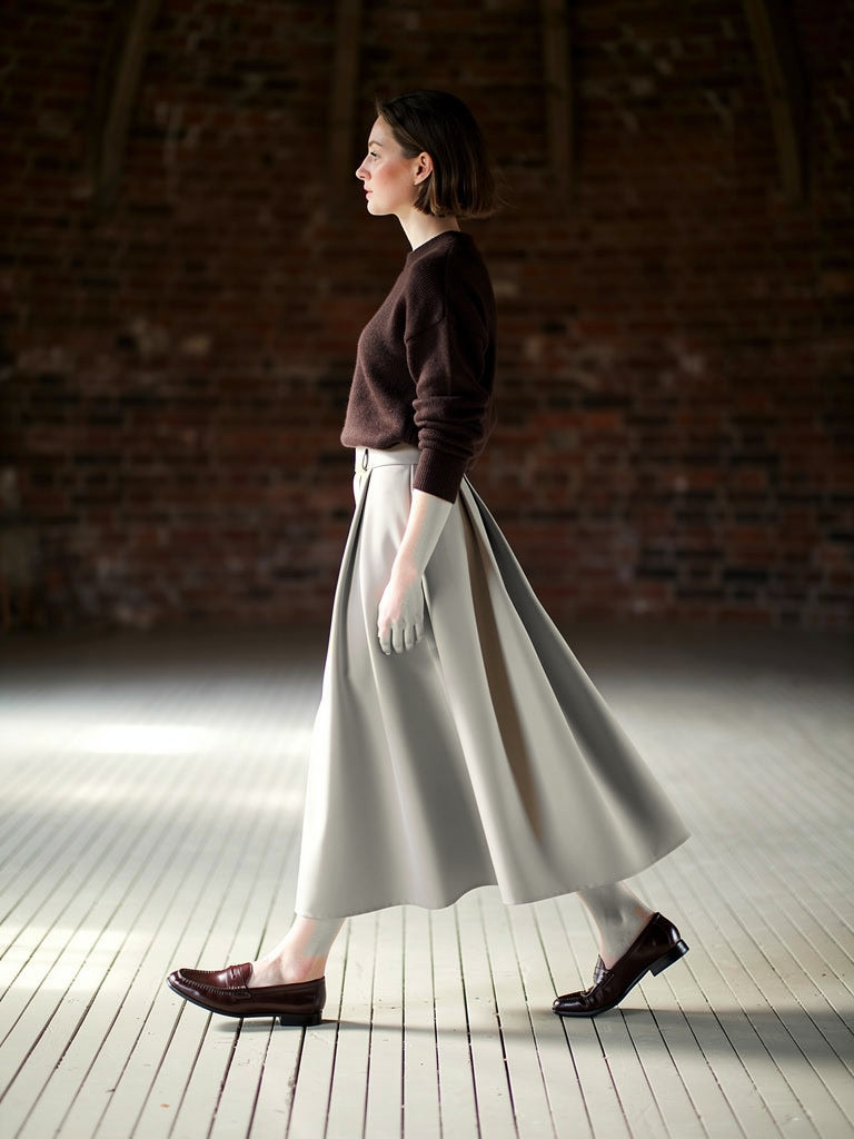 Pleated midi skirt in greige, worn walking with a brown knitted jumper and loafers