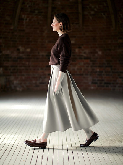 Pleated midi skirt in greige, worn walking with a brown knitted jumper and loafers