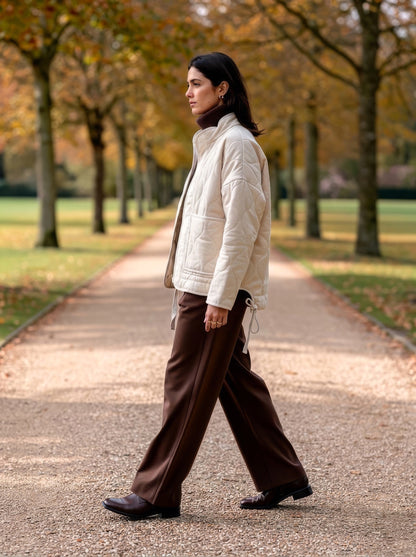 Ecru quilted jacket worn over a brown rollneck on an autumn beech avenue
