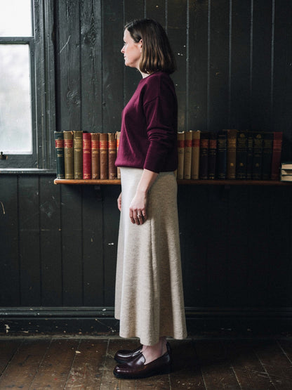 Side view of the porridge ribbed midi skirt in wear, the hem falling low on the calf, photographed in a panelled village reading room