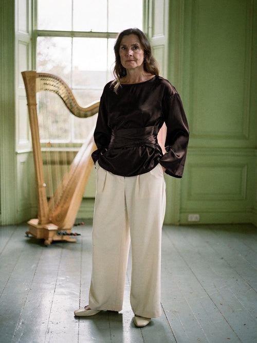 Woman wearing the chocolate satin blouse, wide boat neck, flared sleeves and tie sash