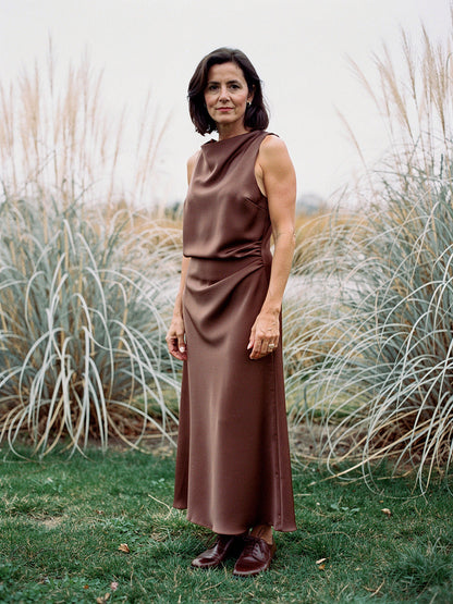 Woman wearing a Pecan brown satin maxi dress with a draped cowl neck in an autumn grass garden