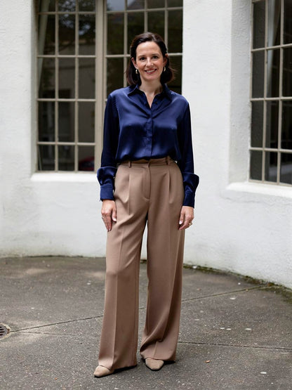 Woman wearing a navy satin shirt tucked into wide leg trousers in a white modernist courtyard