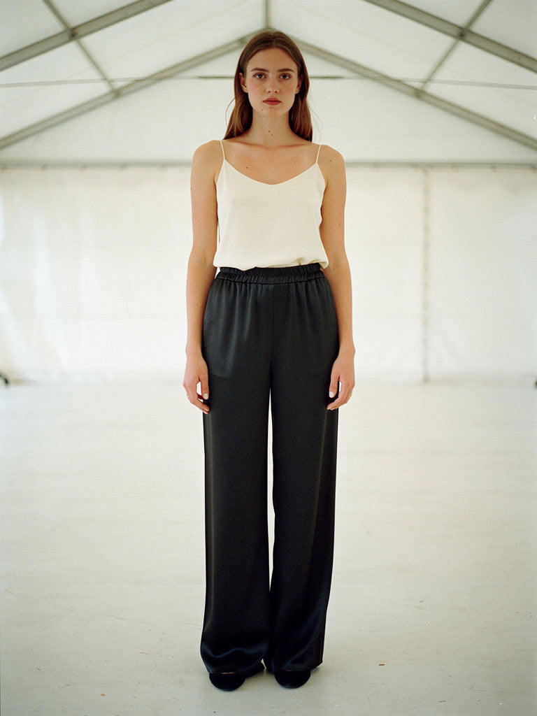 Woman in black satin trousers with an ivory camisole, shown full length