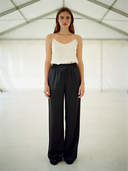 Woman in black satin trousers with an ivory camisole, shown full length