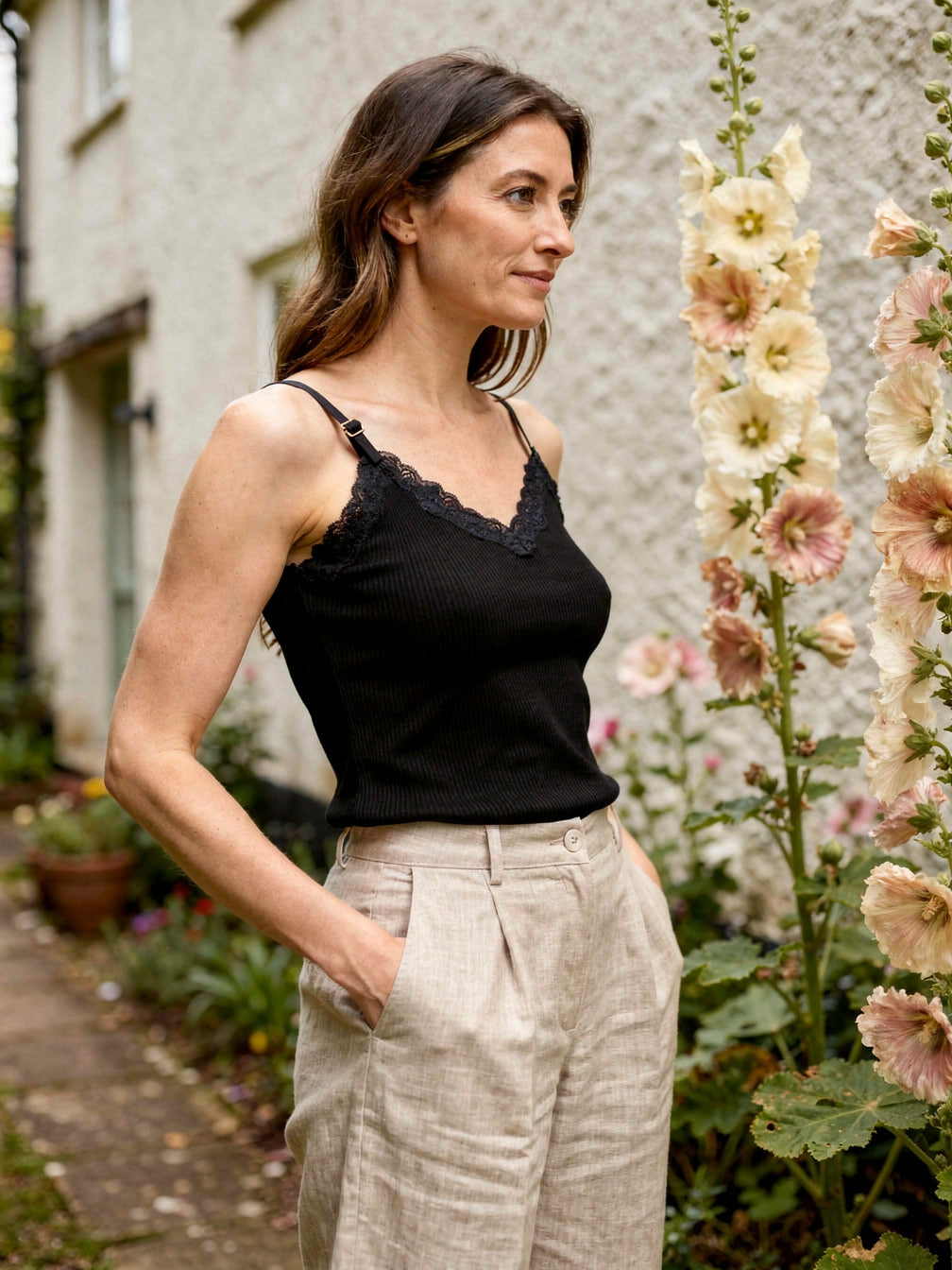 Side view of the jet black silk cami with lace trim, beside cottage hollyhocks