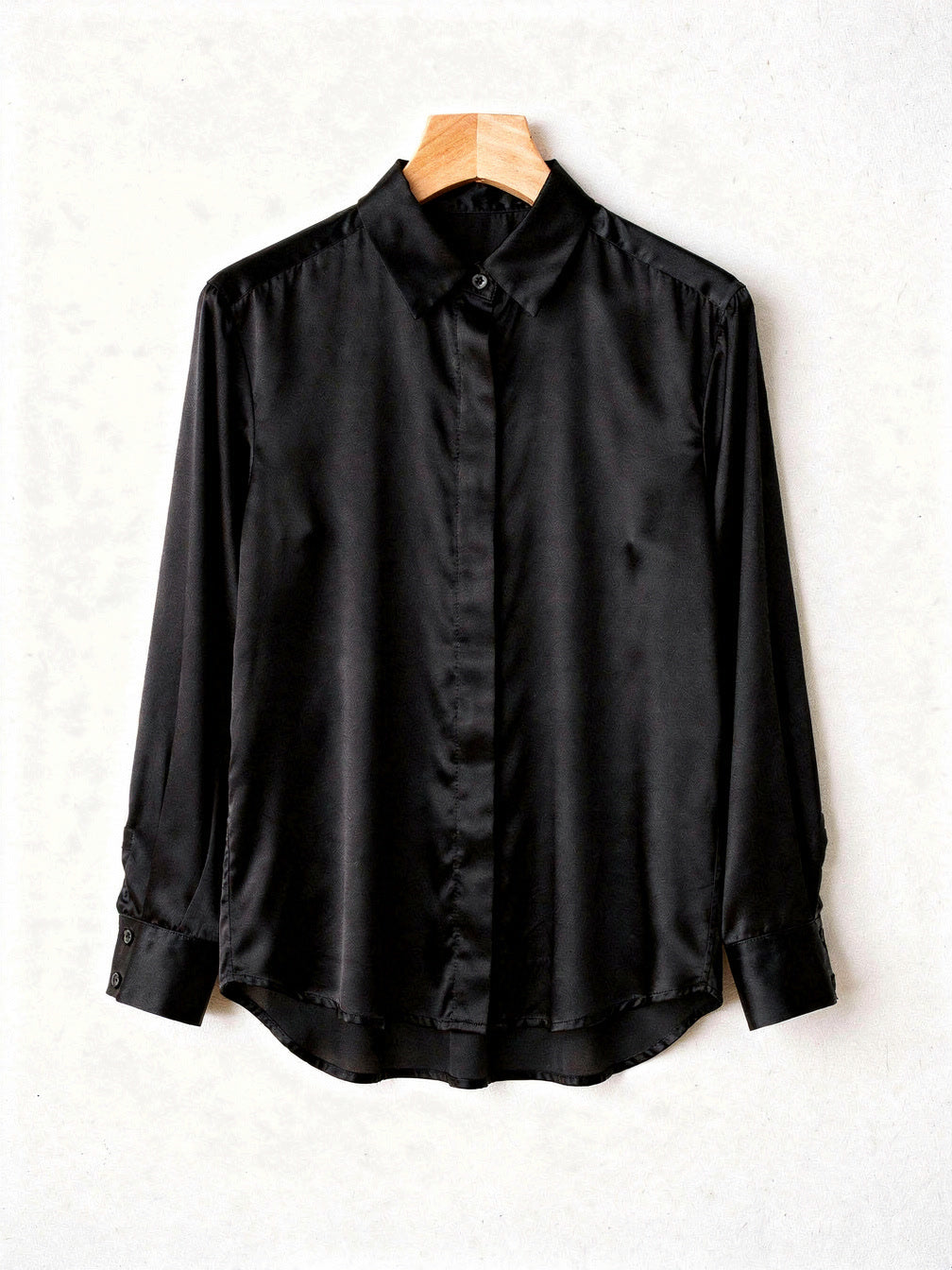 Black silk shirt on a wooden hanger showing the point collar and concealed placket