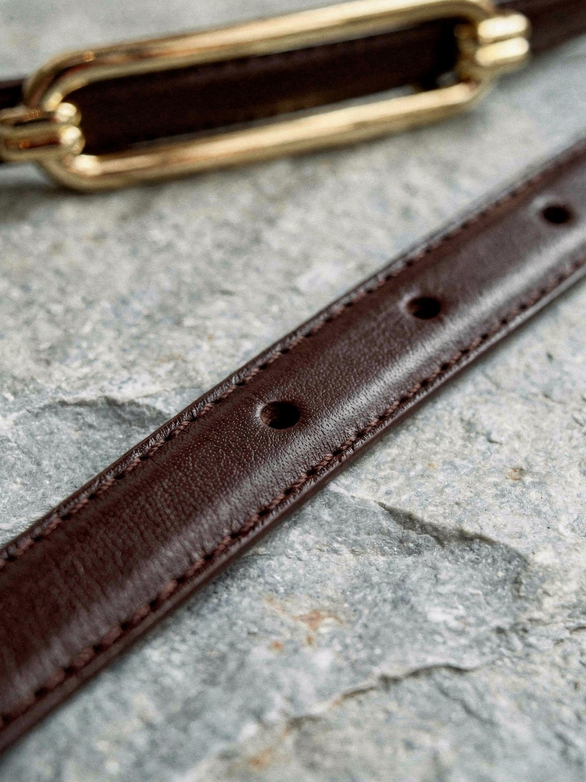 Close detail of the skinny belt strap, its edge stitching, burnished edge and bare punch holes