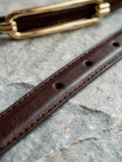 Close detail of the skinny belt strap, its edge stitching, burnished edge and bare punch holes