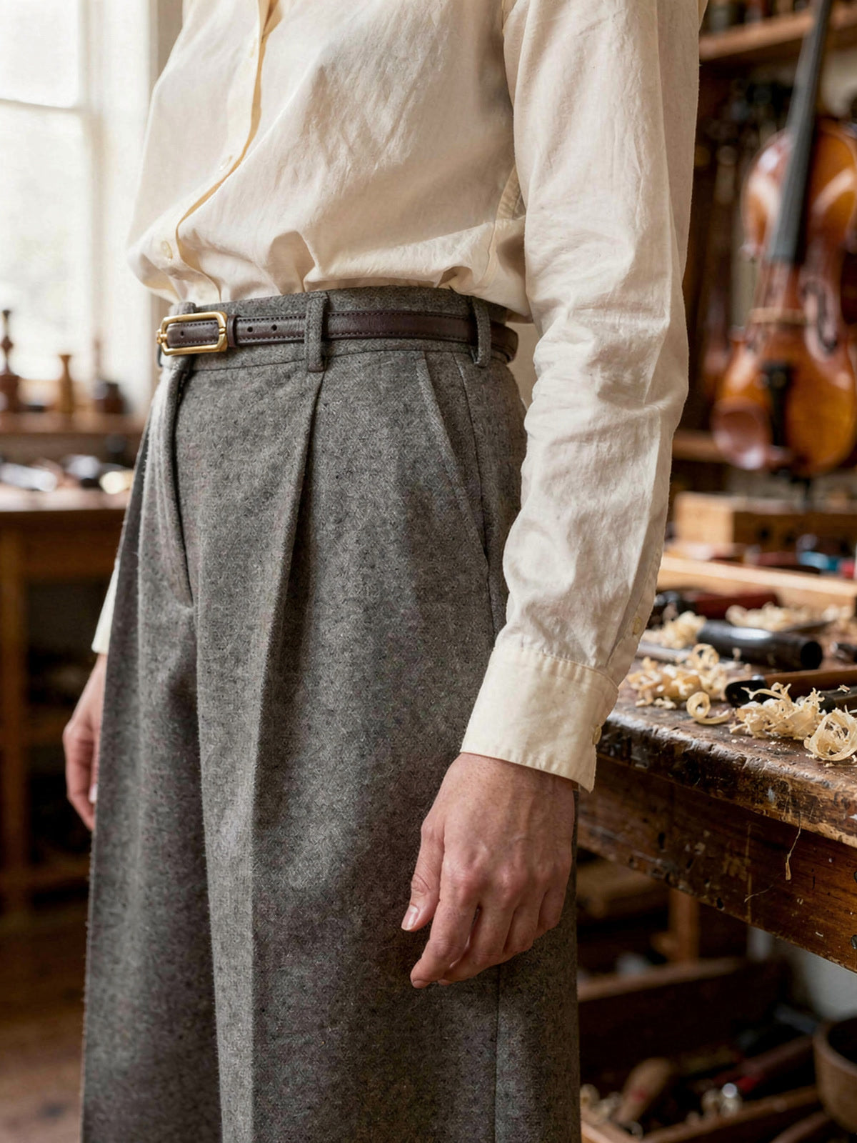 Skinny cow leather belt worn at the waist of grey wool trousers, seen from the side