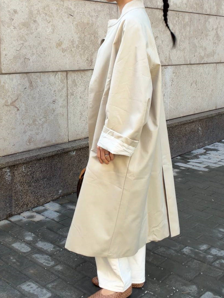 Side view of the stand collar coat in Sesame, showing the longline cocoon cut and the mid calf hem