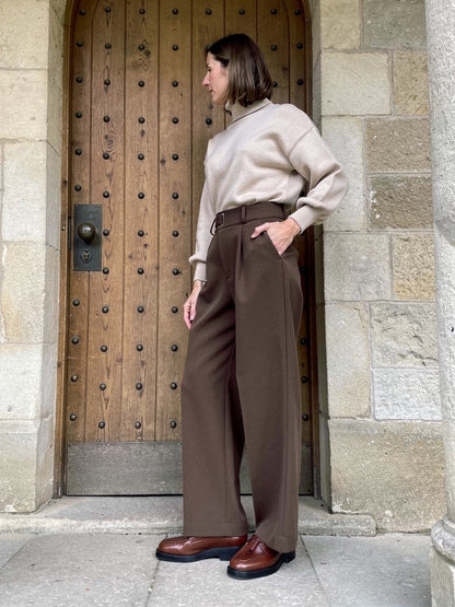 Side view of the straight-leg tailored trousers in Muscovado, worn with a roll neck in a stone porch
