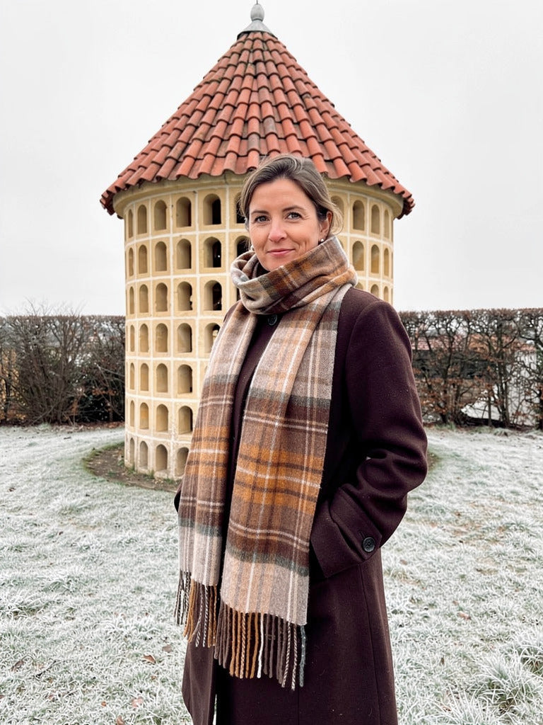 Woman wearing a brushed wool tartan scarf in Bracken Check over a dark brown winter coat