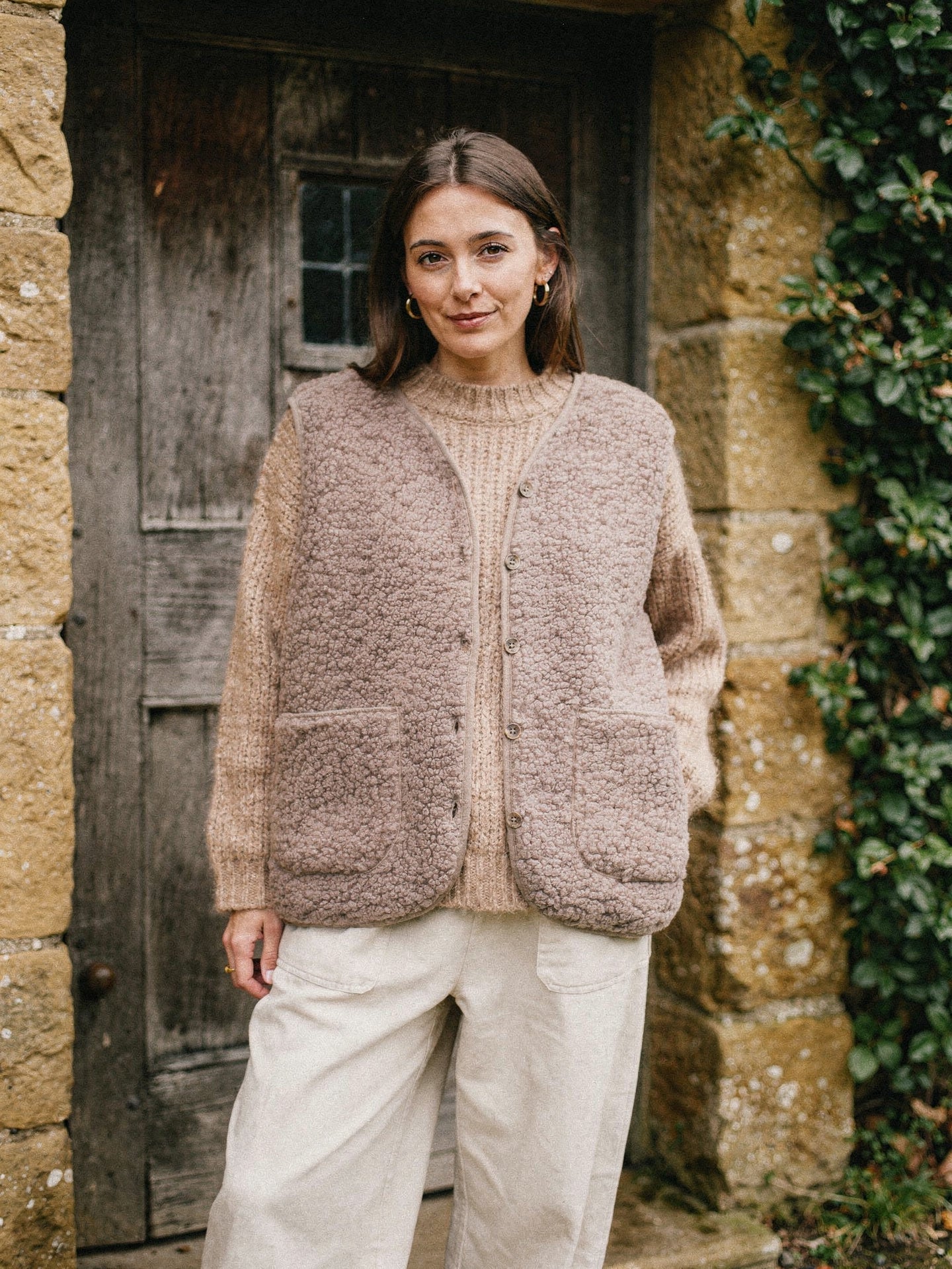 Mocha teddy gilet layered over an oatmeal jumper in a cottage porch
